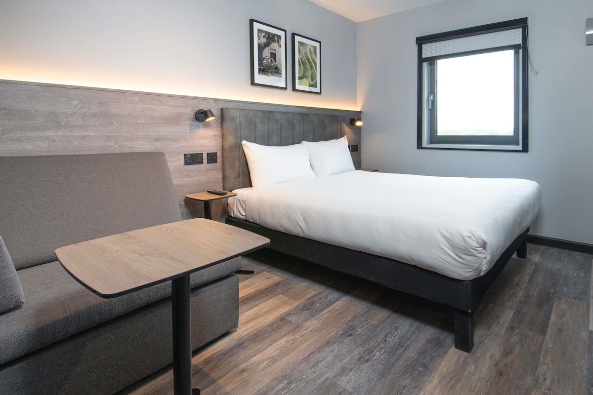 Een moderne hotelkamer met een bed, een bank, een eettafeltje en een raam.