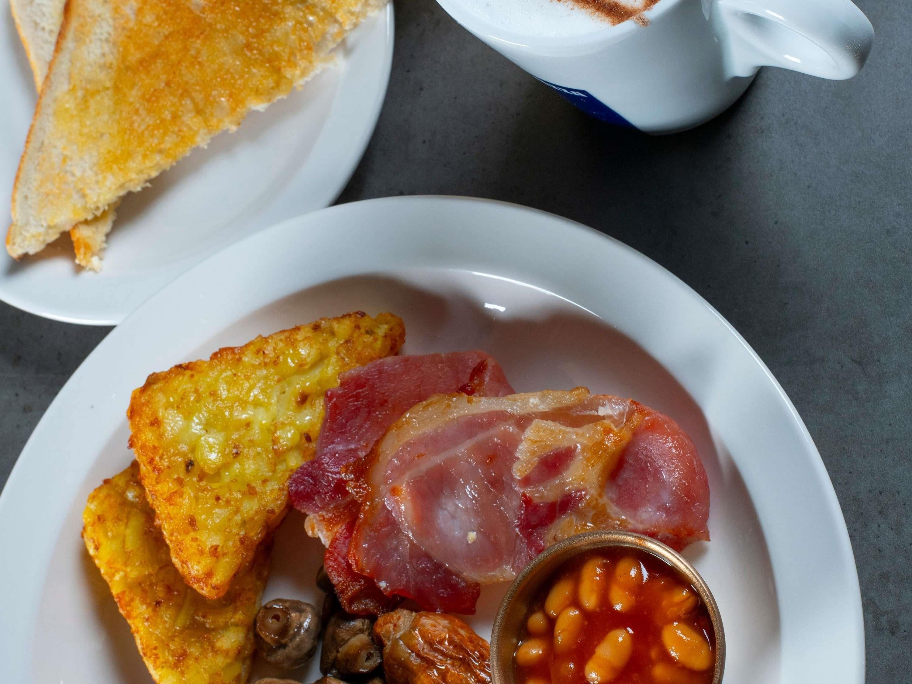 A plate with toast, bacon, beans, and a cup of coffee.
