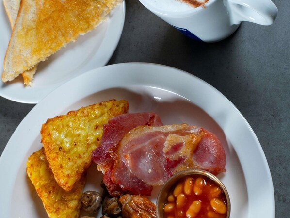 A plate with toast, bacon, beans, and a cup of coffee. - Ibis Styles London Gatwick Airport (Crawley)