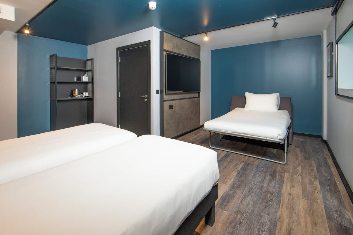 Een hotelkamer met twee bedden, een kledingkast, een televisie en een plank met toiletartikelen.