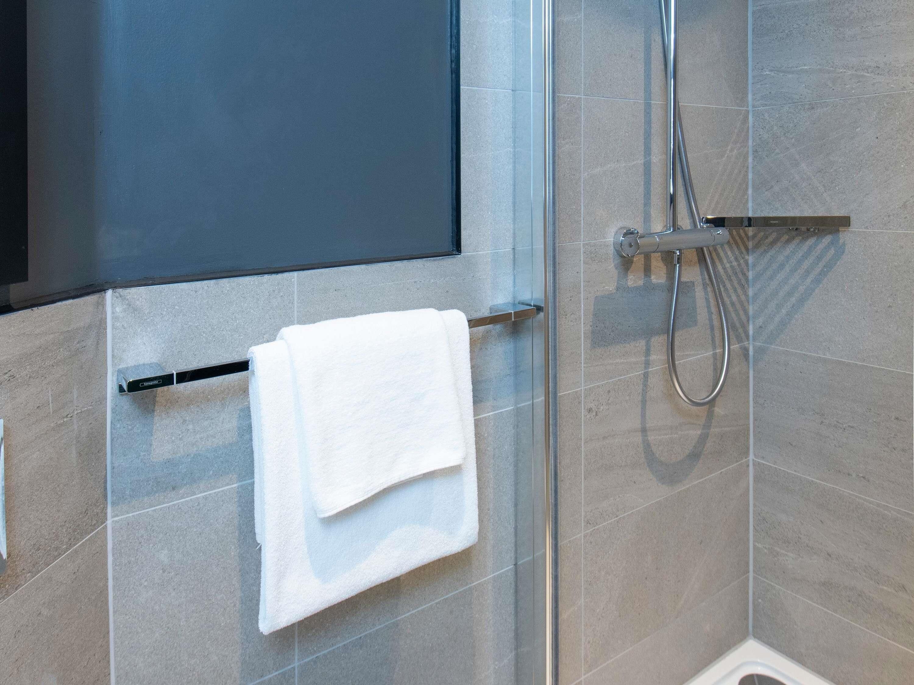 A shower with a handheld showerhead and a towel rack with a folded towel.