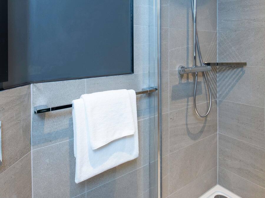 Een douche met een handdouche en een handdoekrek met een opgevouwen handdoek.