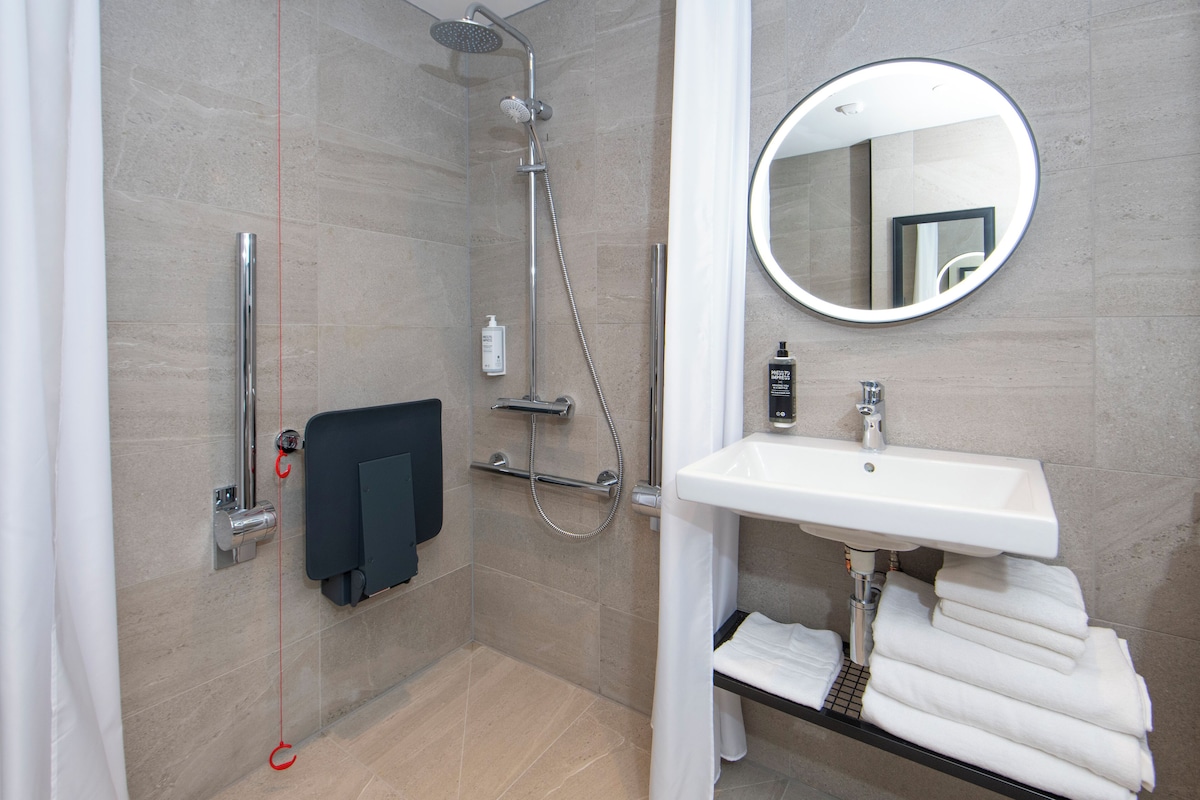 Un baño moderno con ducha, lavamanos, espejo y toallero.
