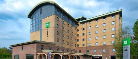 A hotel with a modern design, featuring a prominent glass facade, a brick lower section, and a car park.