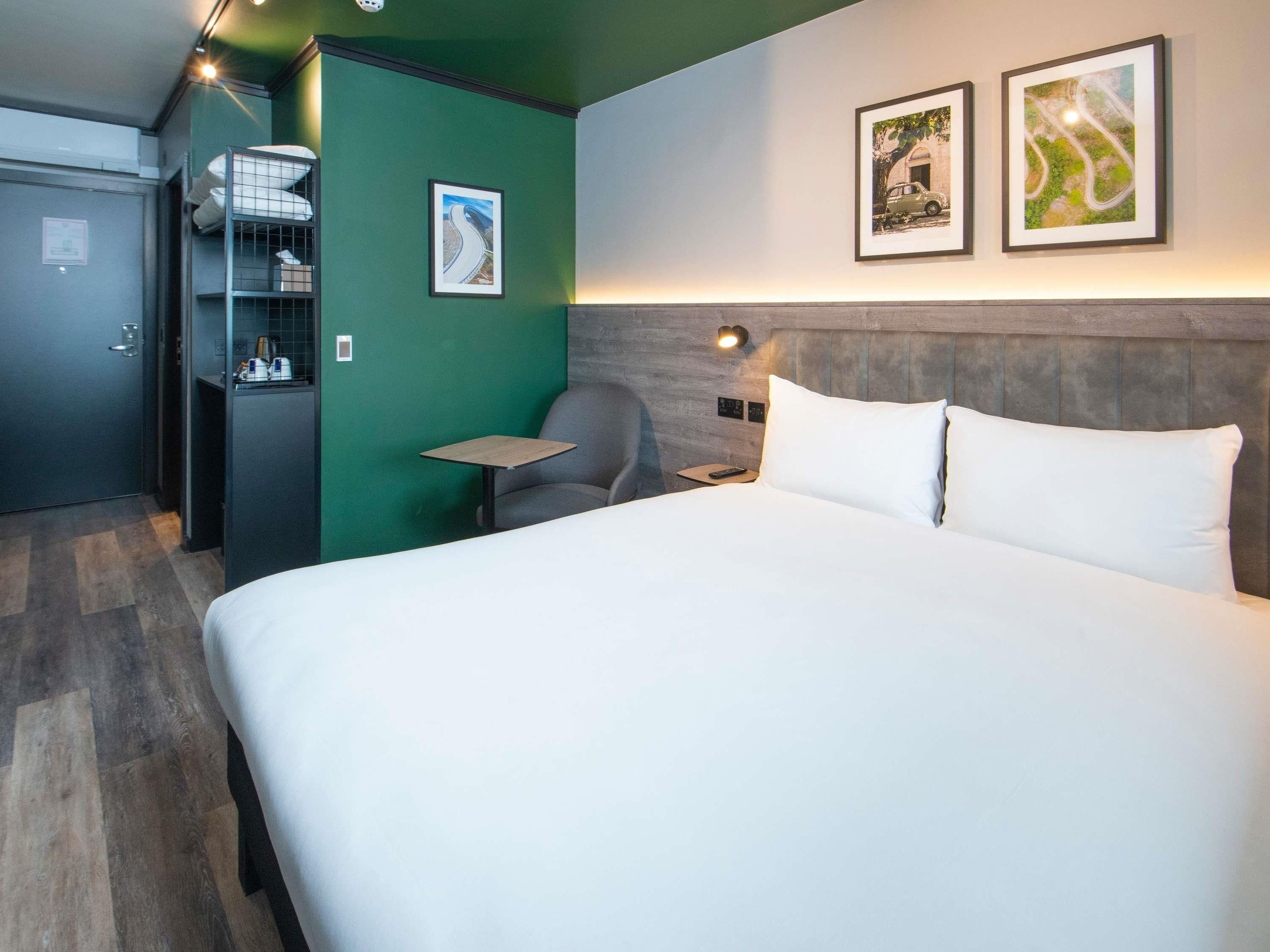 A hotel room with a large bed, a desk, a chair, and two framed pictures on the wall.