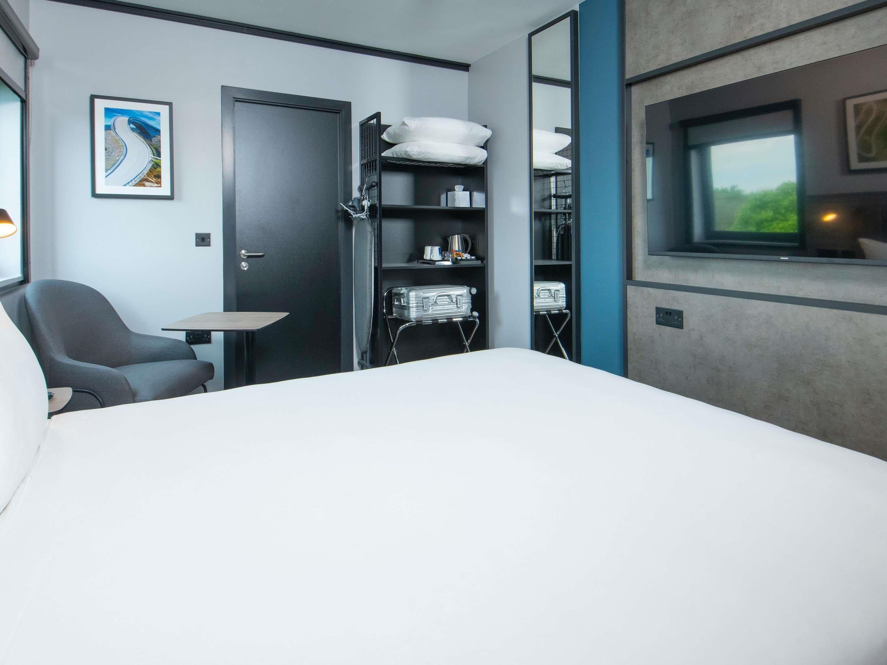 A hotel room with a bed, a chair, a small table, a wardrobe, and a window.