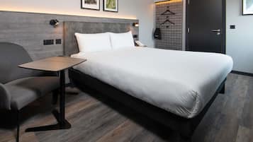 A modern hotel room with a large bed, a small table, a chair, a wardrobe, and a door.