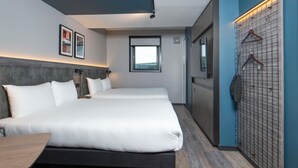 Une chambre d’hôtel avec deux lits, un bureau, une armoire et un porte-manteau fixé au mur.