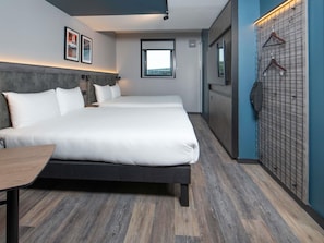Een hotelkamer met twee bedden, een bureau, een kledingkast en een wandkapstok.