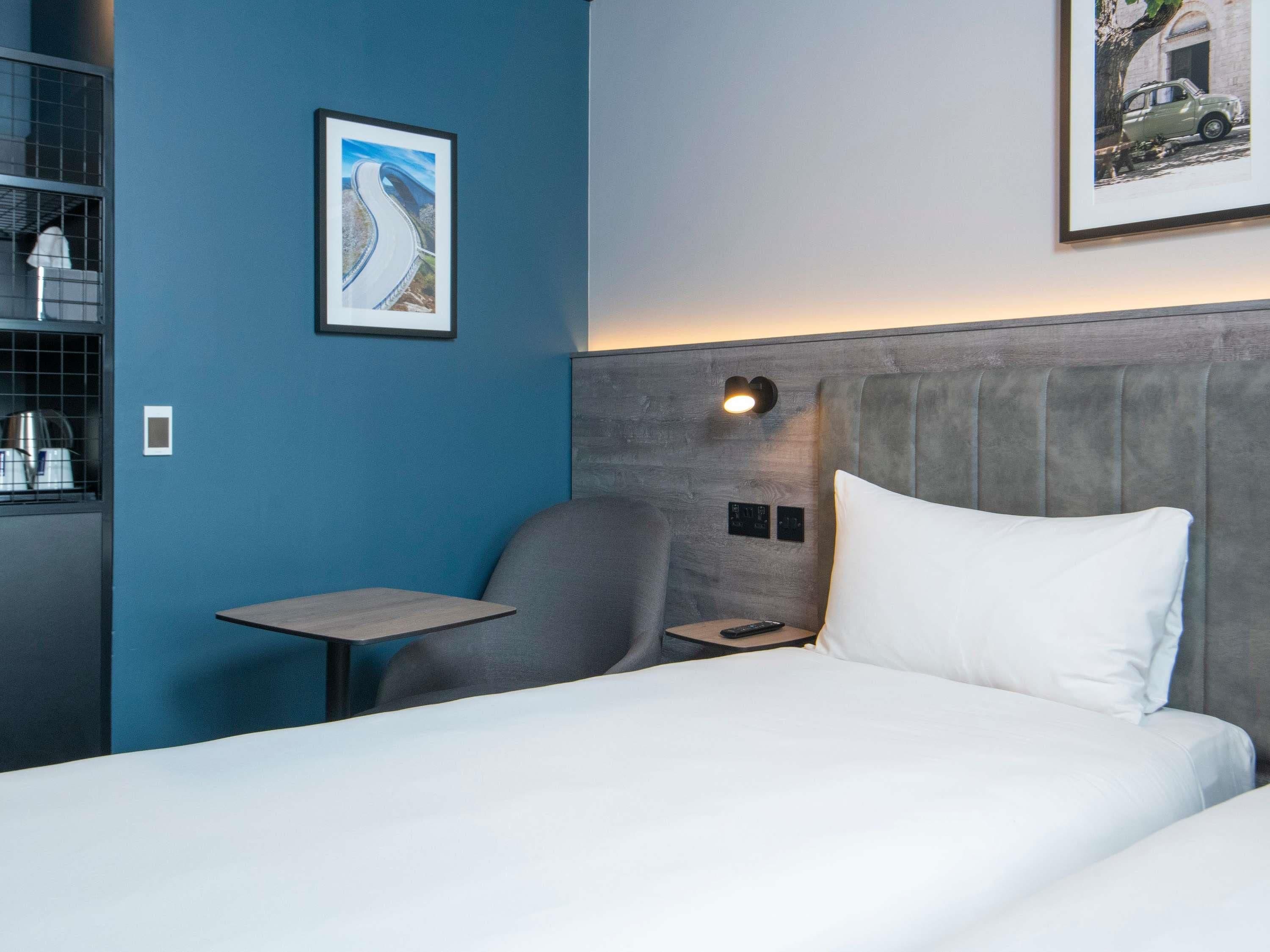 Une chambre d’hôtel équipée d’un lit, d’un bureau, d’une chaise et d’une lampe fixée au mur.