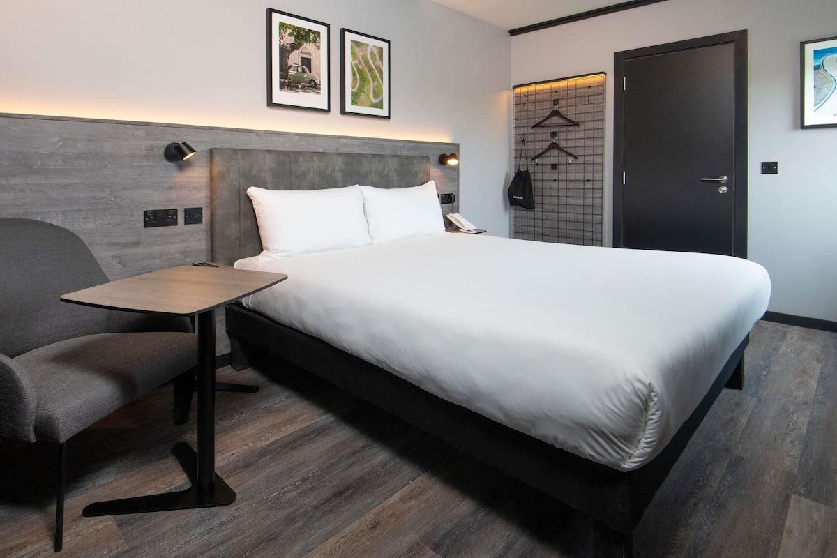Een moderne hotelkamer met een groot bed, een klein tafeltje, een stoel, een kast en een deur.