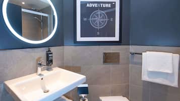 A bathroom with a white sink, a mirror with a circular light, a framed compass sign, a toilet, and a towel rack.