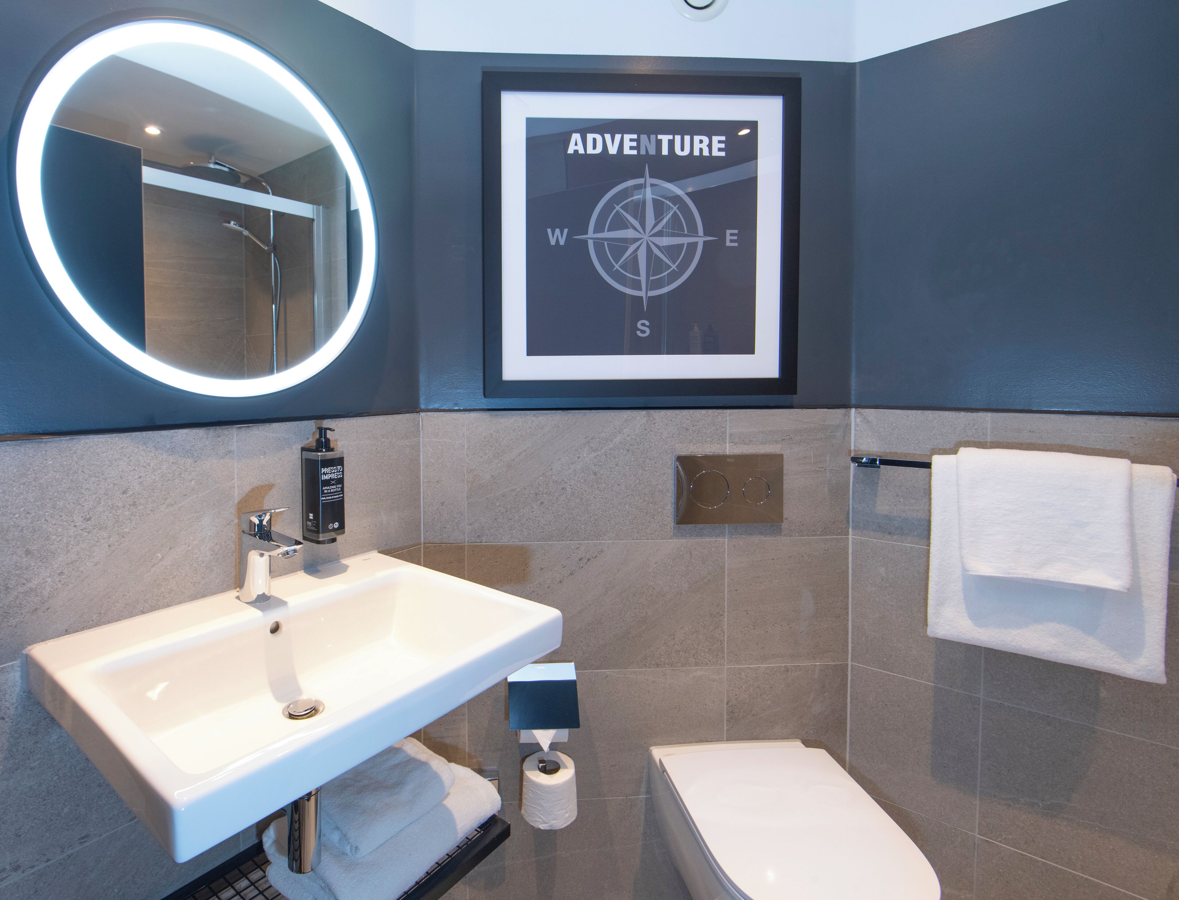 Un baño con lavamanos, espejo, letrero de brújula enmarco y un inodoro.