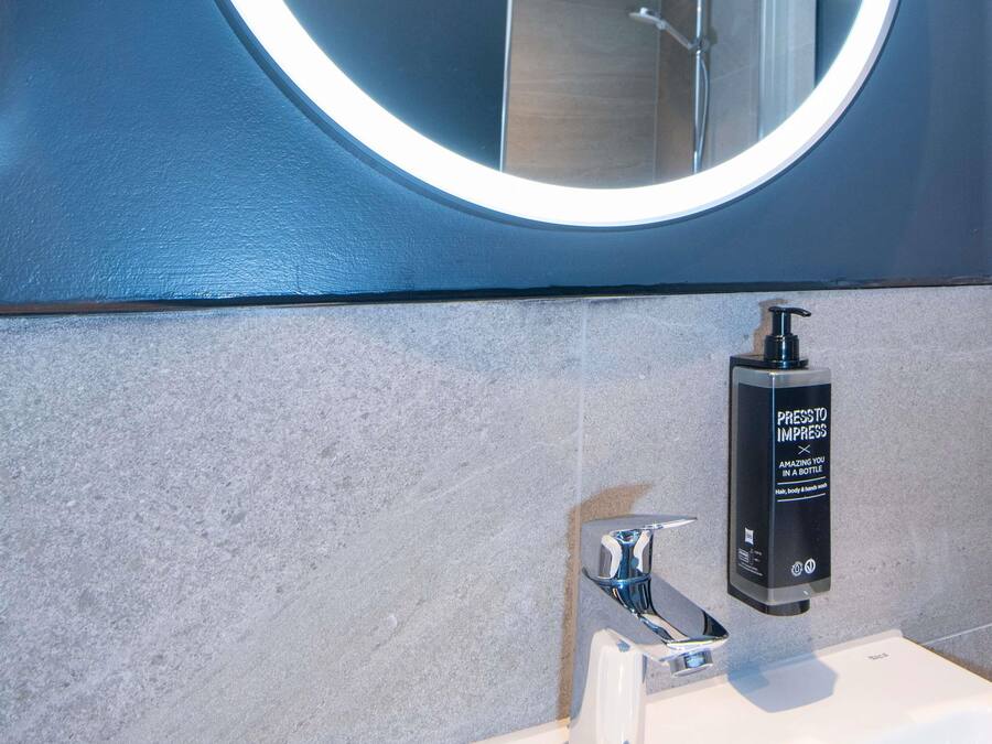 Modernilla designilla varustettu kylpyhuone, jossa on pyöreä peili, seinään kiinnitetty saippua-annostelija ja krominen hana.