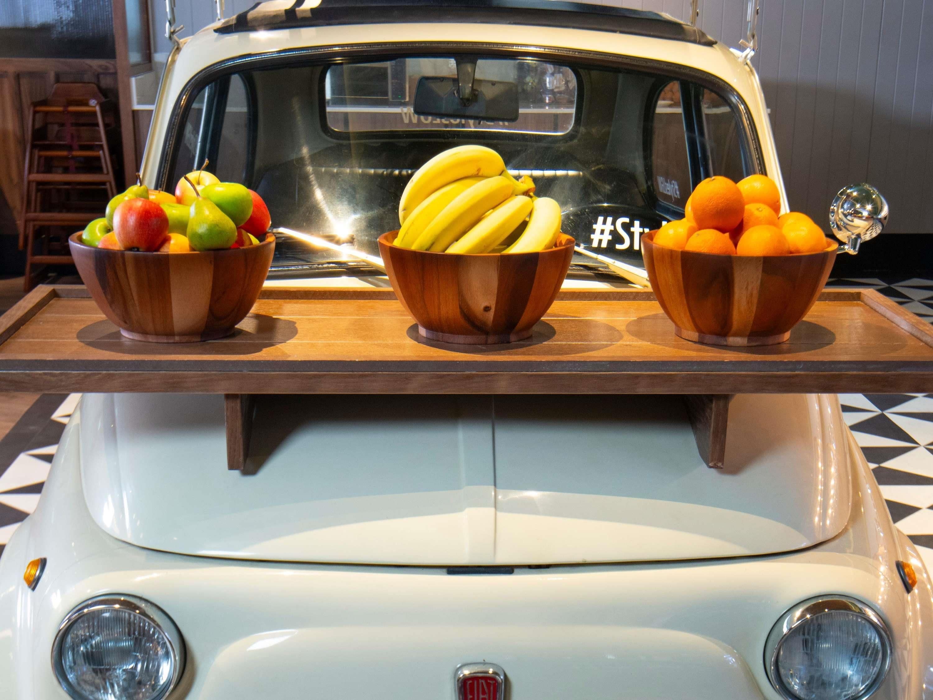 A vintage car with three wooden bowls of fruit on the hood.