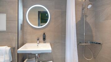 A bathroom with a round mirror, a sink, a shower, and a towel rack.