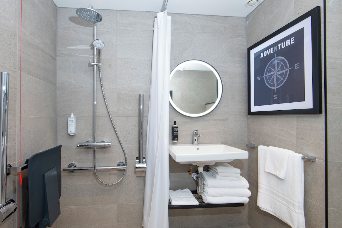 Un baño moderno con ducha, lavamanos y un cartel con brújula enmarcado.