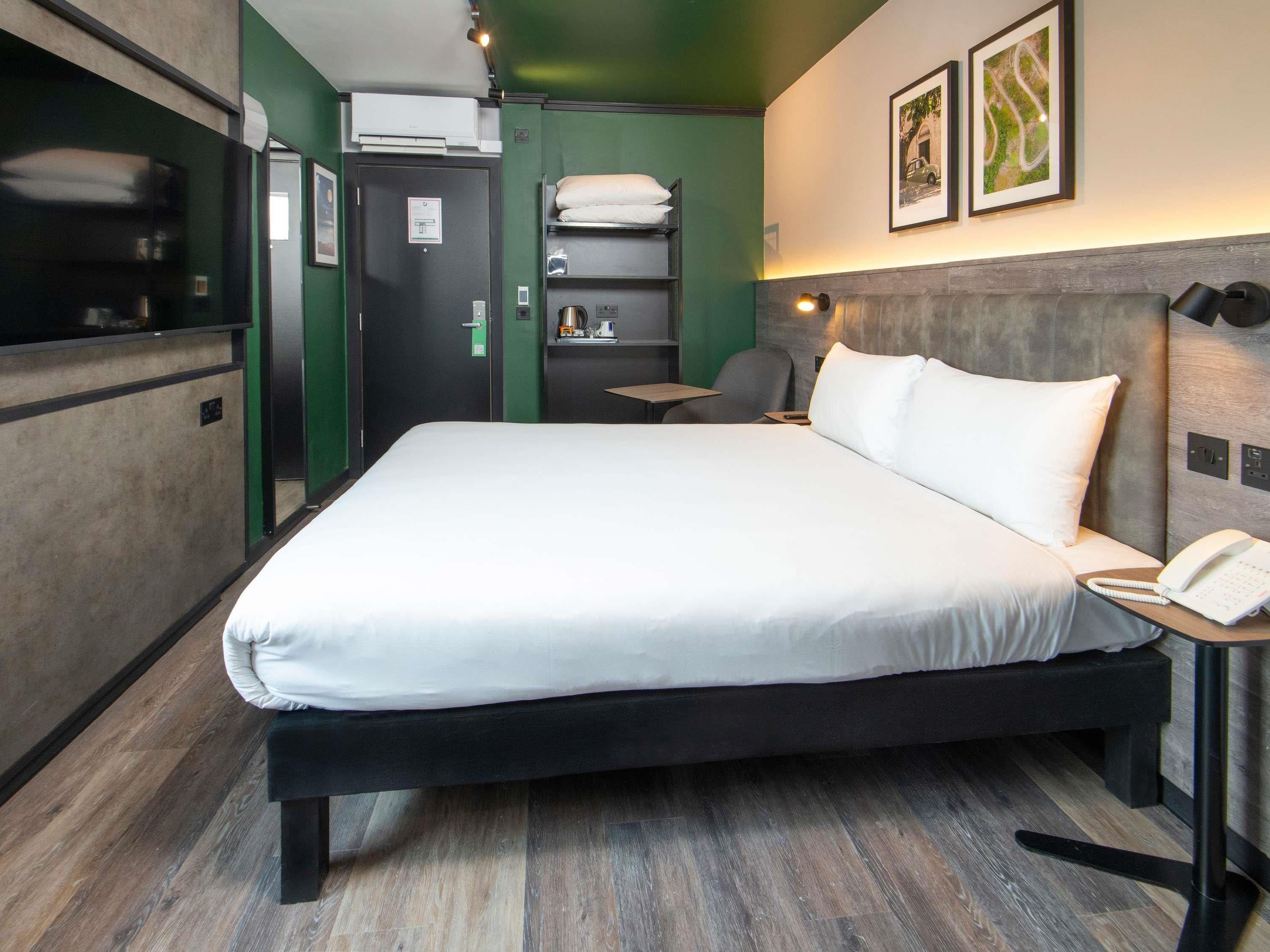 A hotel room with a large bed, a desk, a chair, a phone, and a shelf with towels.