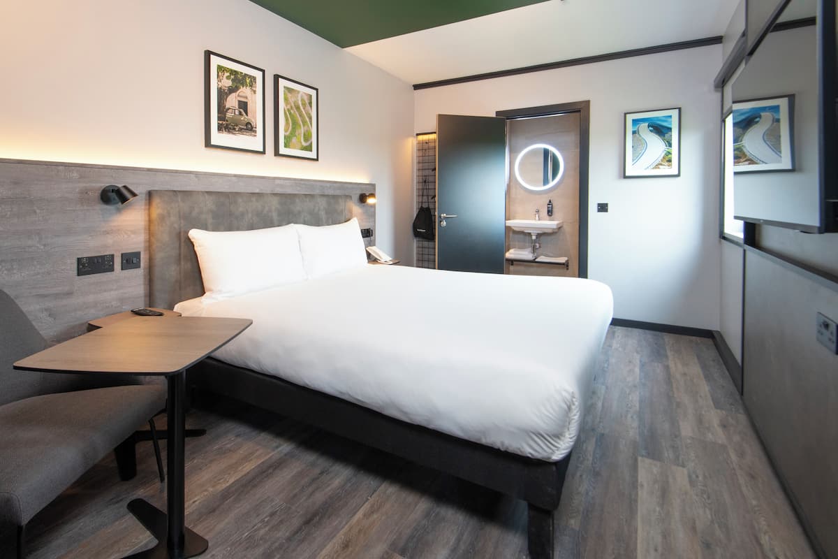 Een moderne hotelkamer met een bed, nachtkastje, stoel en een klein bureau.