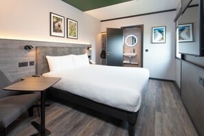 A modern hotel room with a bed, bedside table, chair, and a small desk.