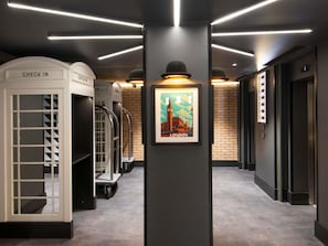 A modern hotel lobby with check-in counters, a framed London poster, and a digital elevator display. - Ibis Styles London Gatwick Airport (Crawley)
