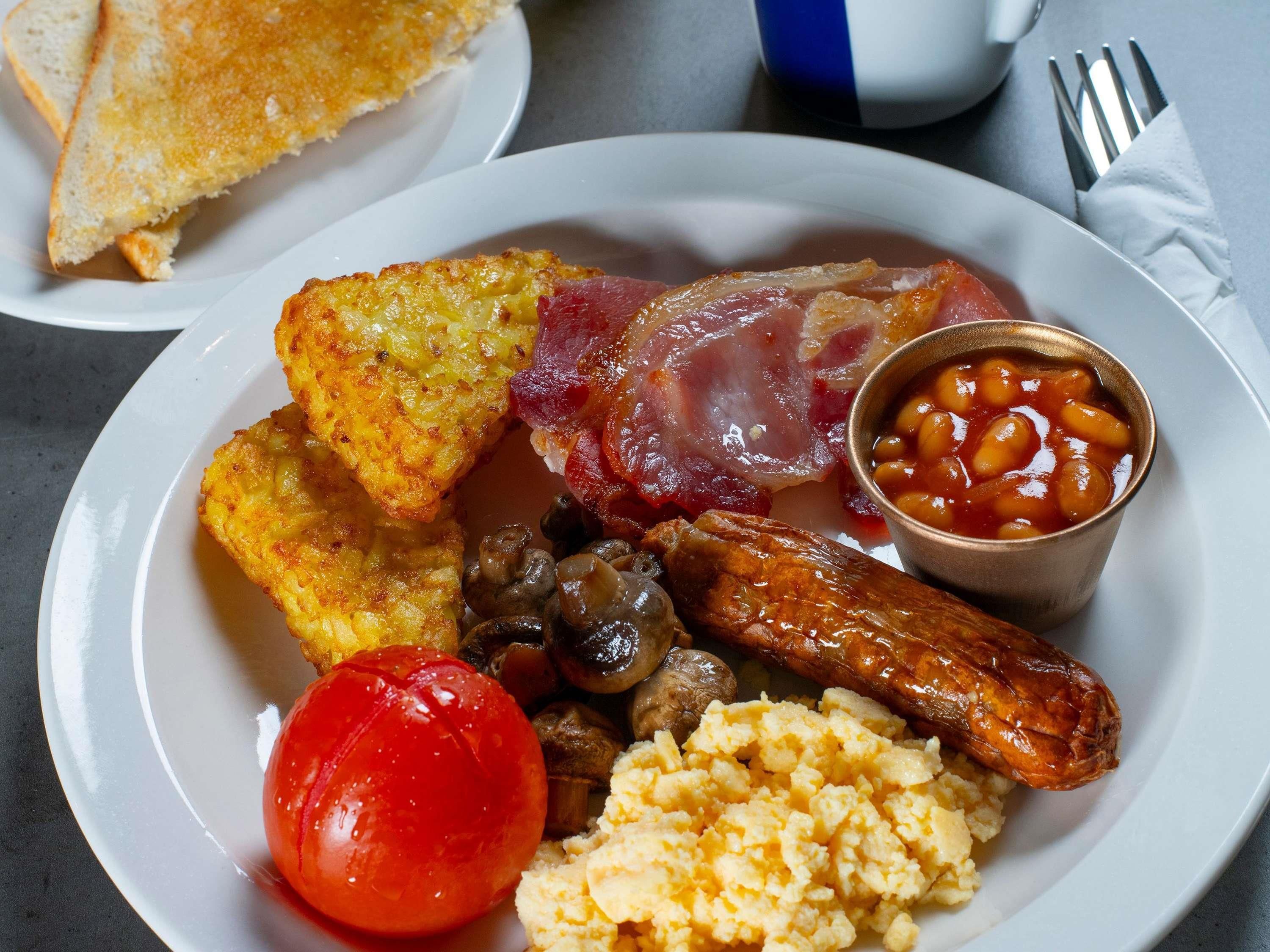 Un plato de comida para el desayuno con tostadas, huevos, tocino, salchichas, champiñones, frijoles y tomate.