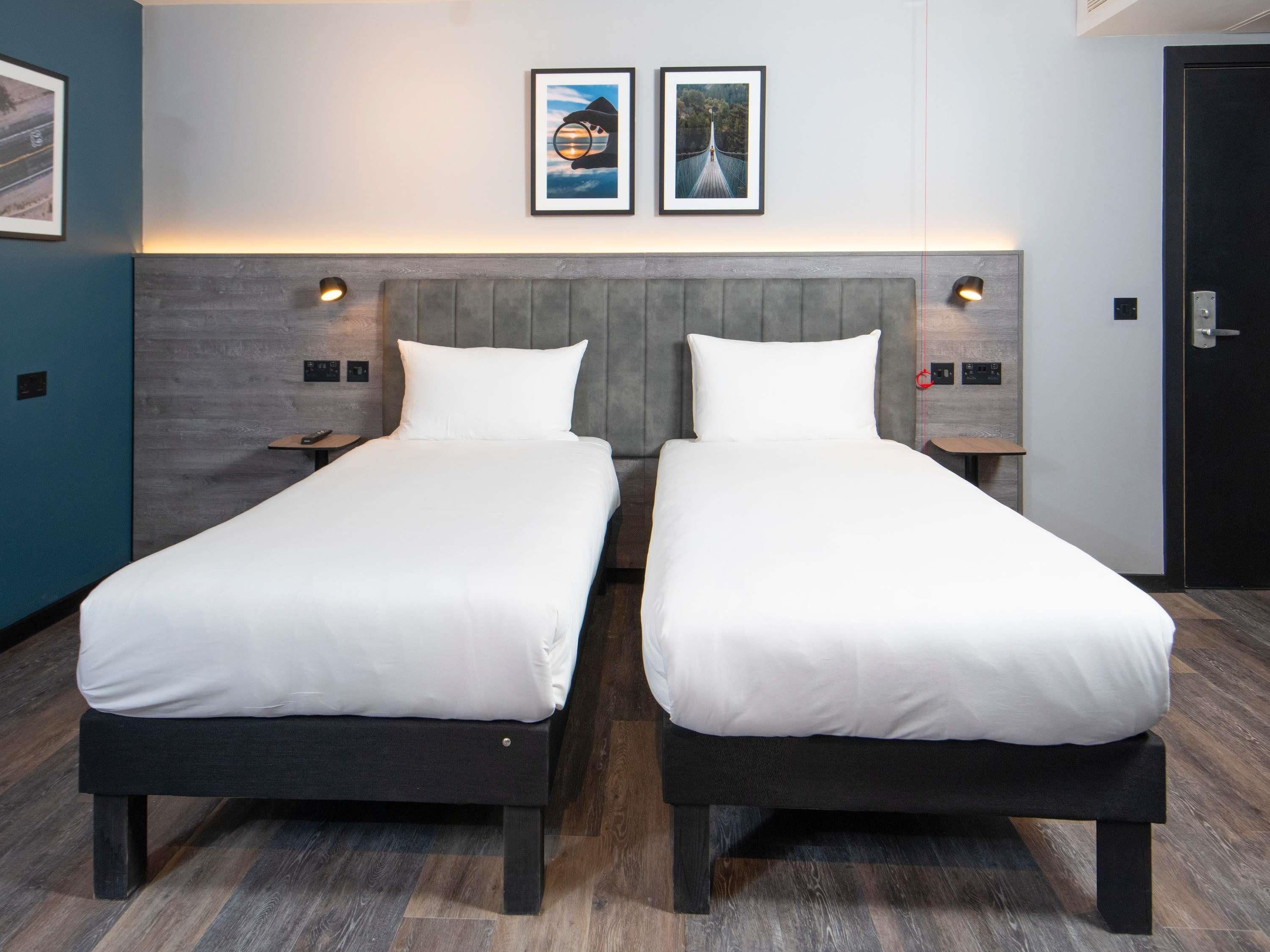 A hotel room with two single beds, a grey headboard, and two framed pictures on the wall.