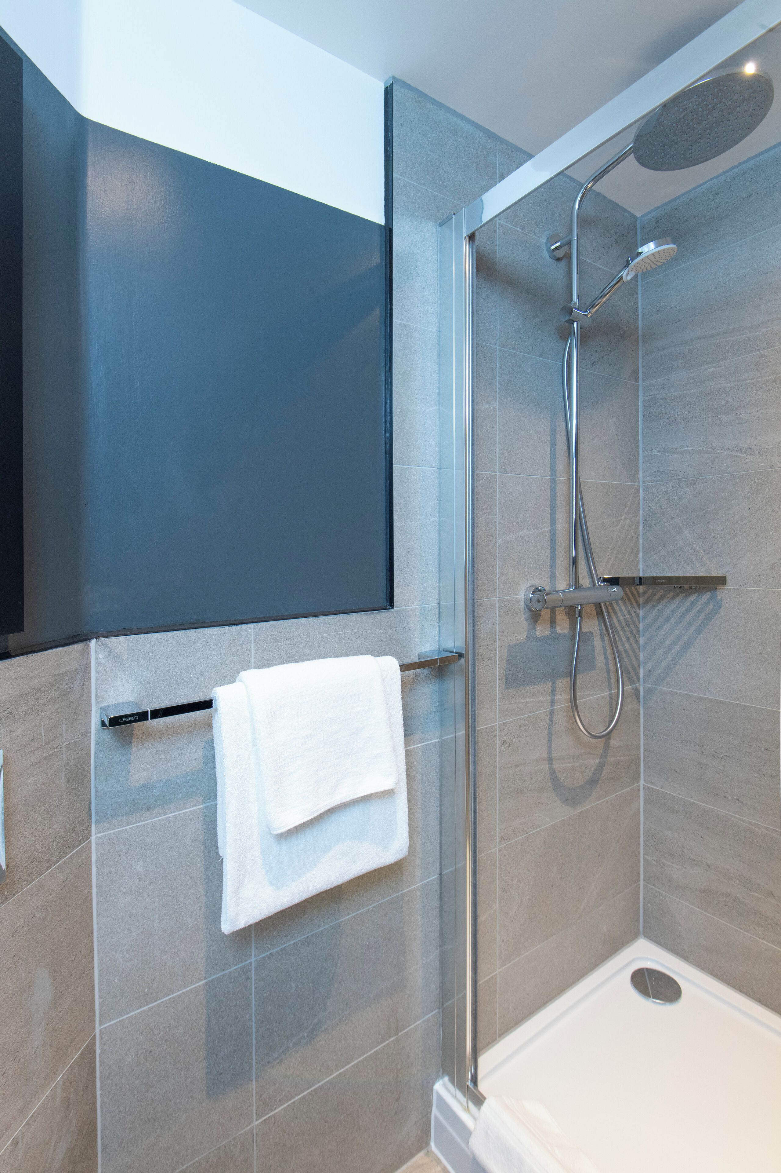 Un espace douche moderne doté d’une paroi en verre, d’un pommeau de douche à main et d’un porte-serviettes avec une serviette blanche.