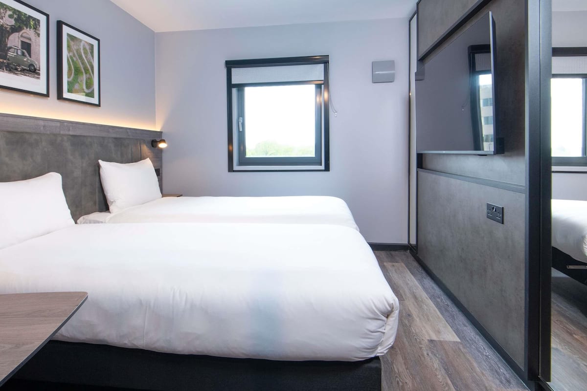 Een moderne hotelkamer met twee bedden, een groot raam en uitzicht op de omgeving.