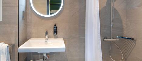 A modern bathroom with a round mirror, a sink, a shower with a handheld showerhead, and a towel rack.