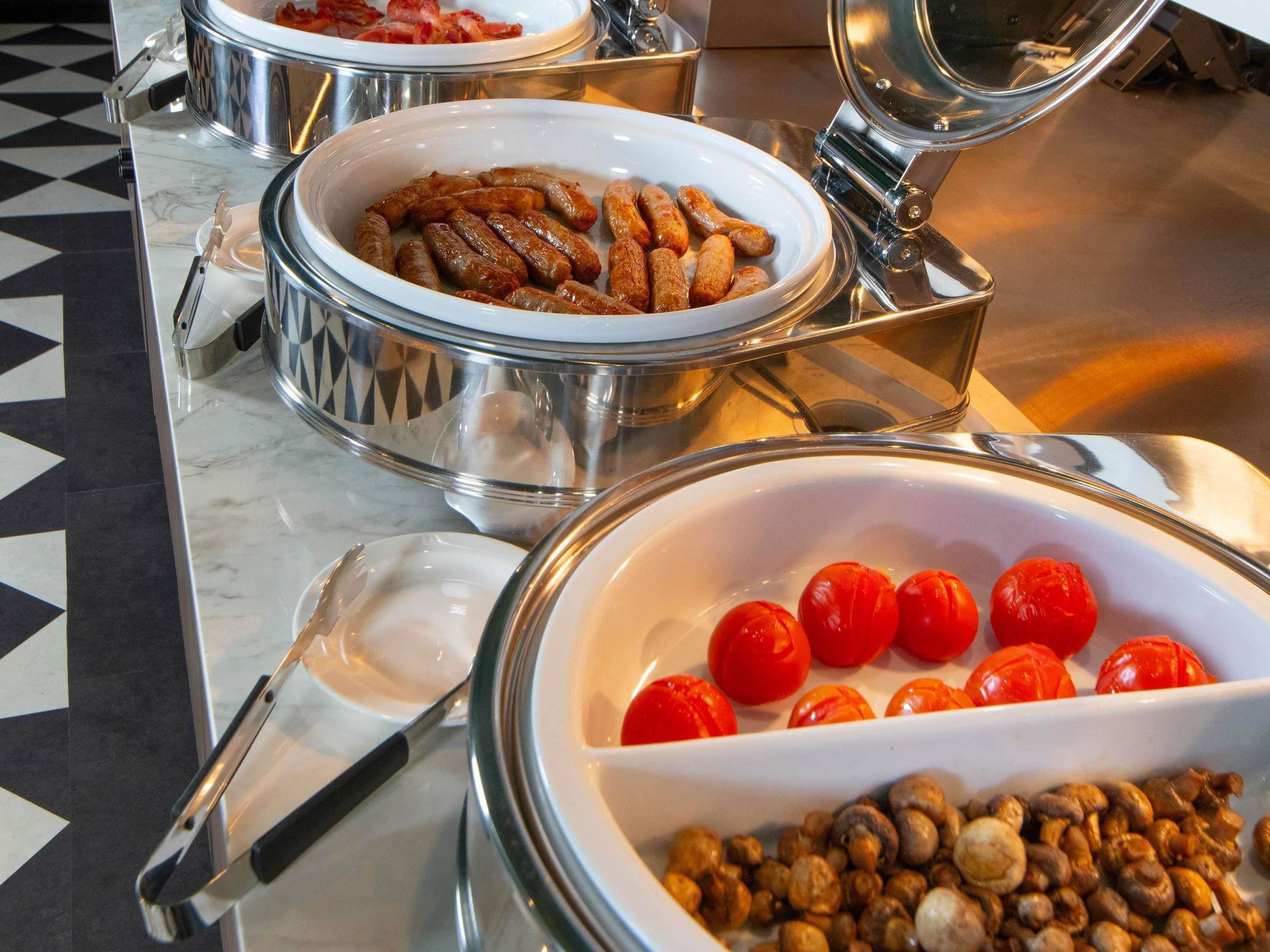 A buffet with various dishes including sausages, cherry tomatoes, and mushrooms.