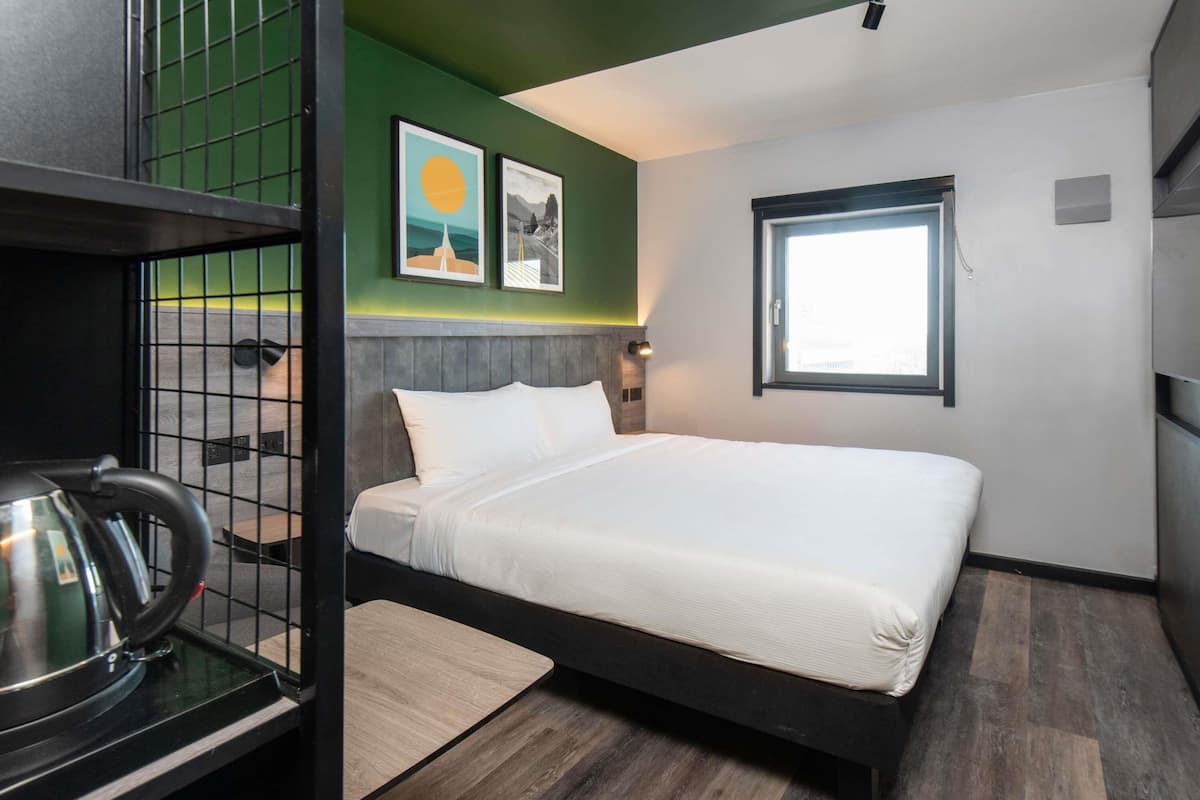 Een hotelkamer met een bed, een waterkoker, een raam en kunst aan de muur.