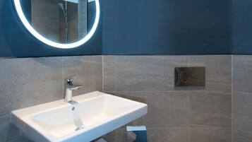 Une salle de bain moderne avec un lavabo blanc, un miroir rond avec un éclairage intégré et un espace douche.