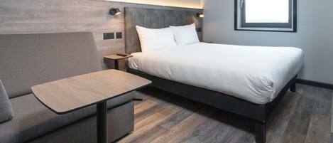 A modern hotel room with a bed, a sofa, a small table, and a window.