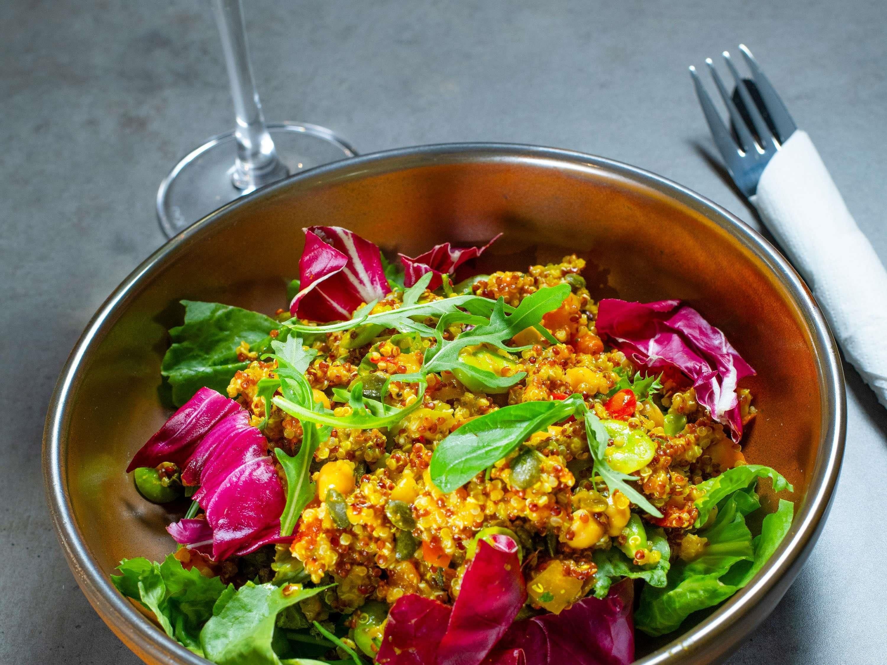 A bowl of quinoa salad with mixed vegetables and greens.