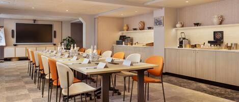 A conference room with a long table, chairs, a projector screen, and a kitchenette area.
