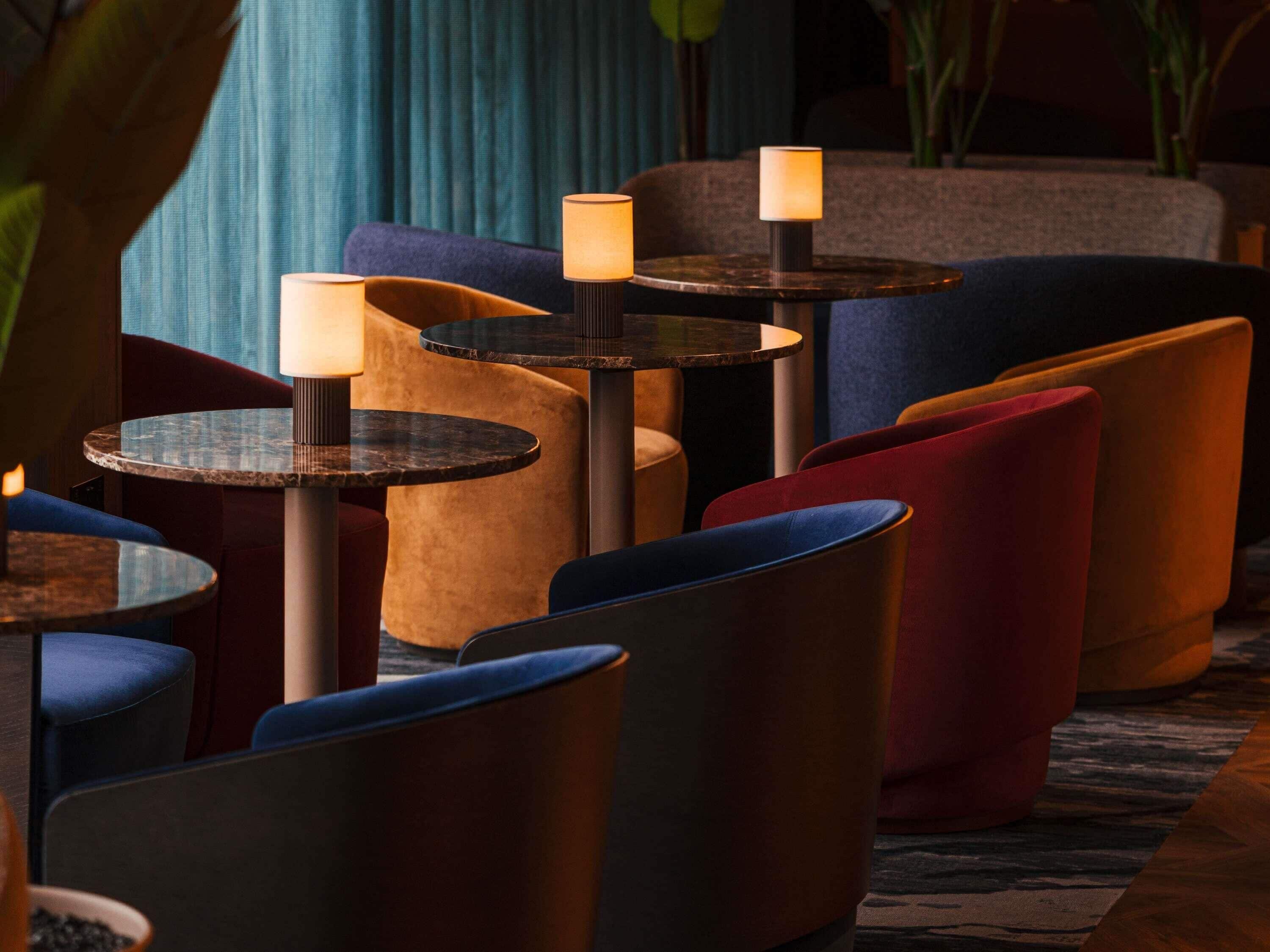 A seating area with round tables and cushioned chairs, some with lamps.