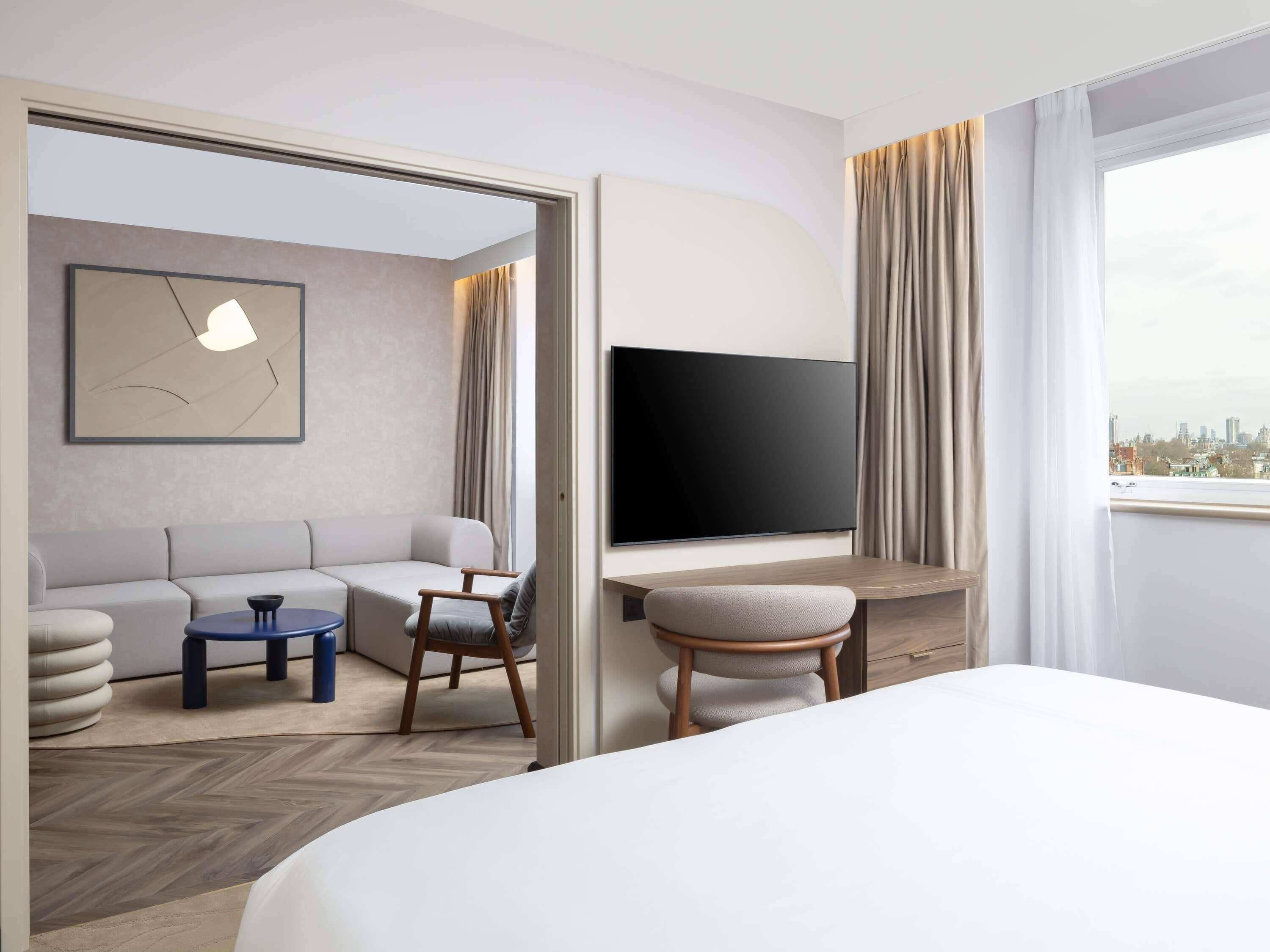 A hotel room with a bed, a sofa, a desk, a chair, a TV, and a city view.