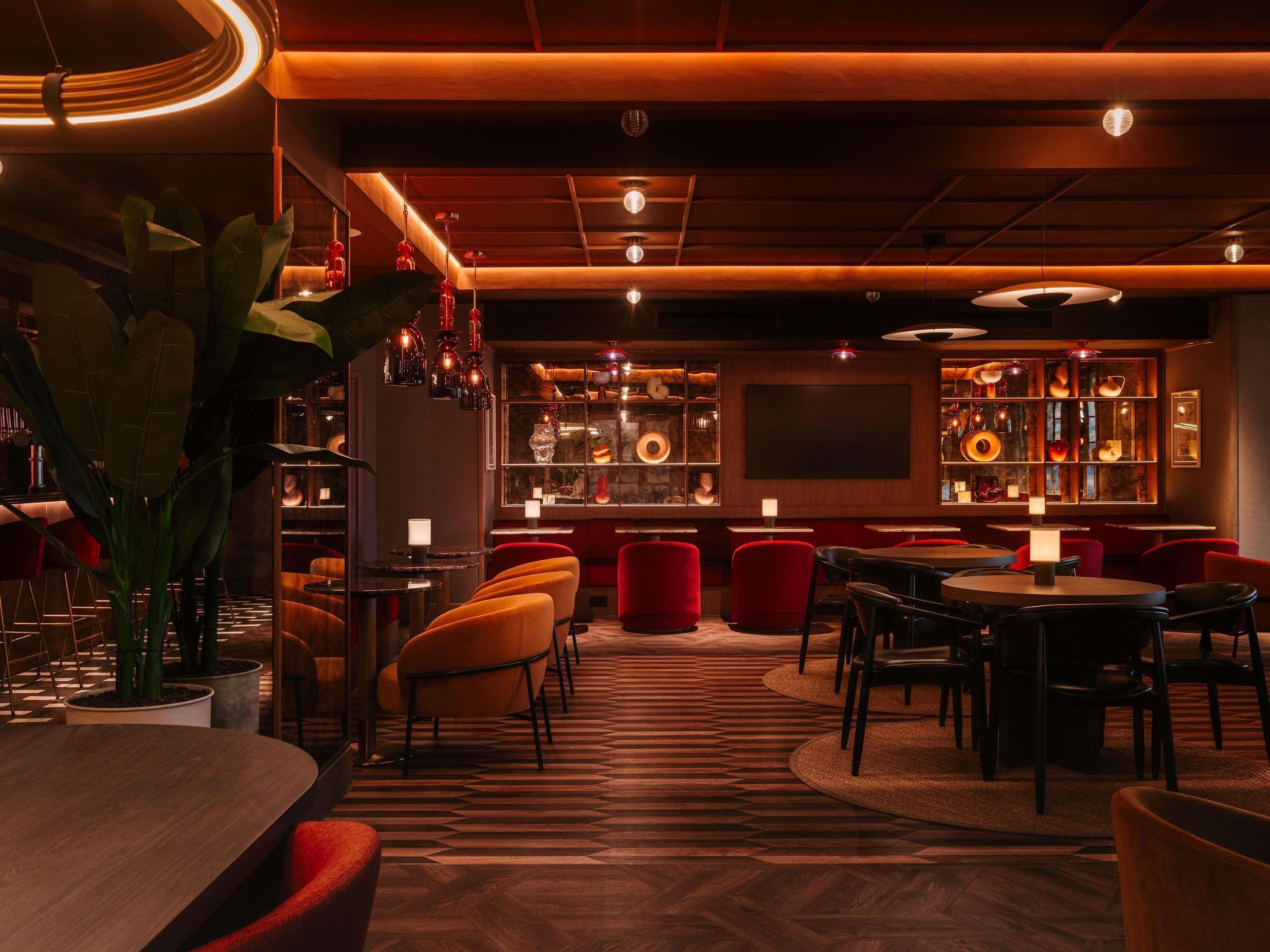 A dimly lit bar area with wooden floors, red chairs, and a variety of decorative items on shelves.