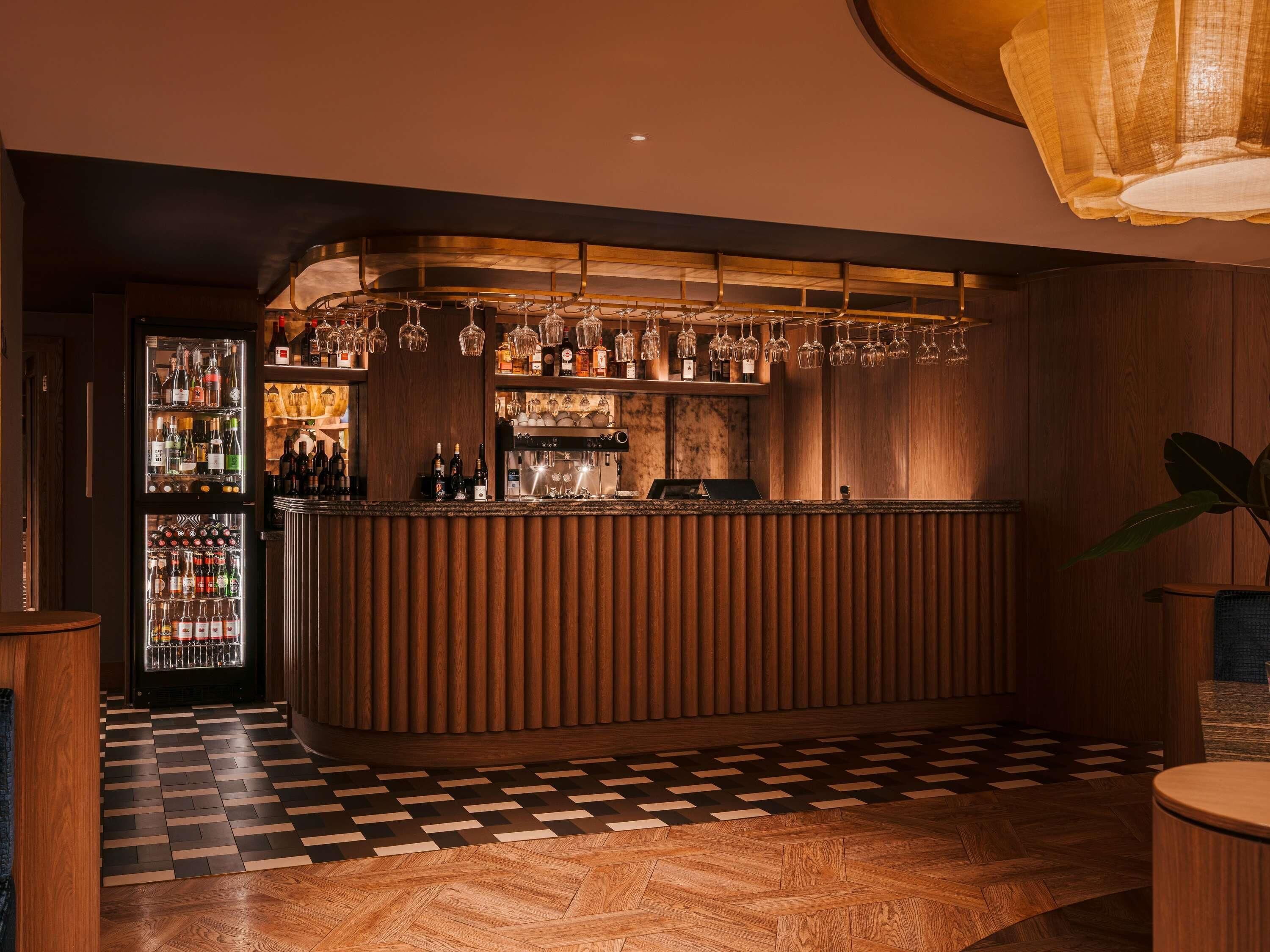 A bar area with a wooden counter, wine glasses, and bottles.