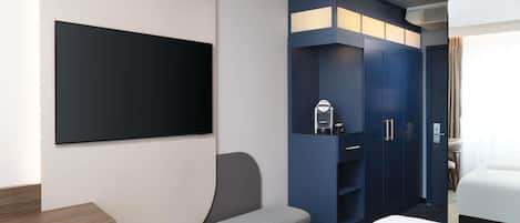 A modern hotel room with a large bed, a small seating area, a built-in wardrobe, and a flat-screen TV.