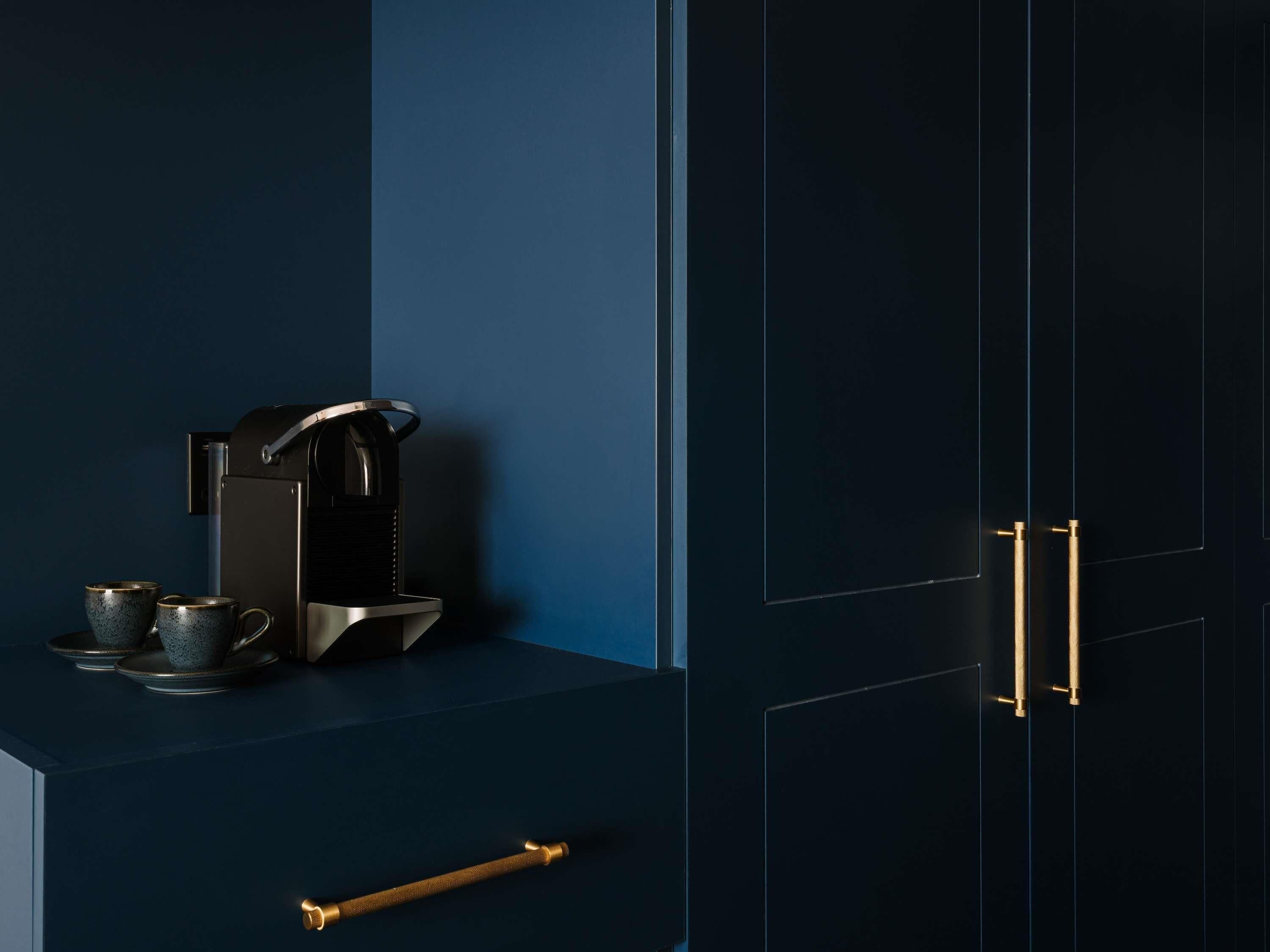 A dark blue cabinet with a coffee maker and two cups on top.