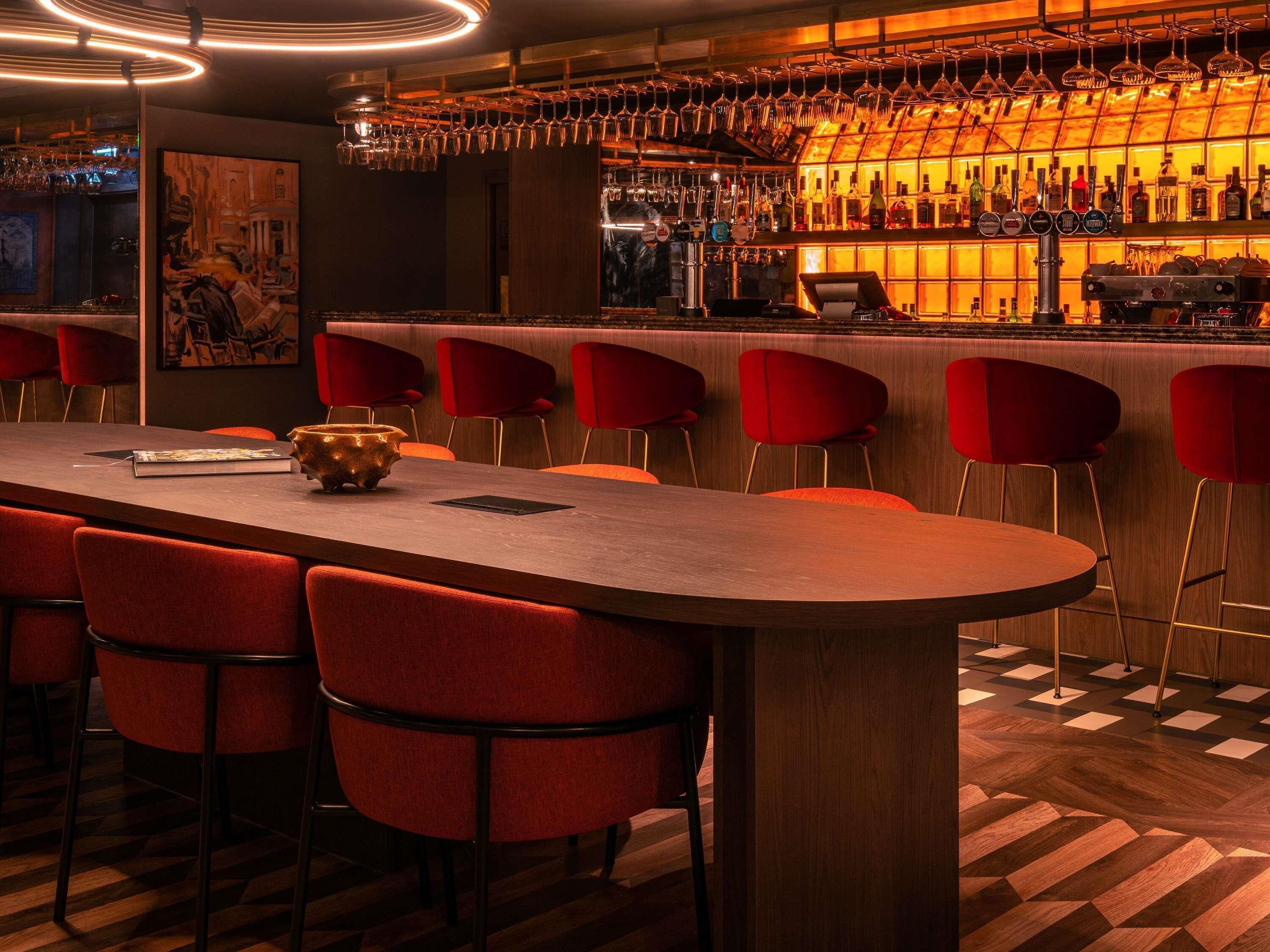 Eine Bar mit einer langen Theke, roten Stühlen und einer Auswahl an Flaschen und Gläsern.