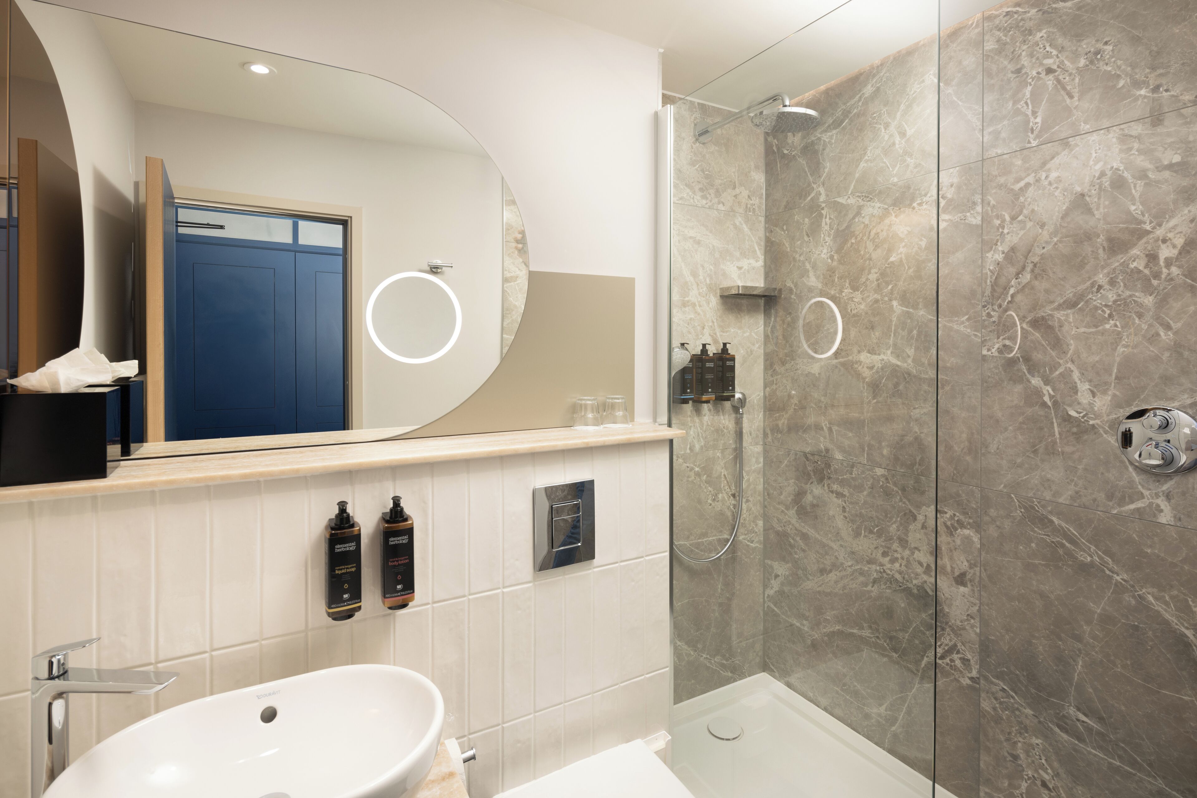 Une salle de bain moderne avec un grand miroir, un lavabo, une douche et une porte bleue.