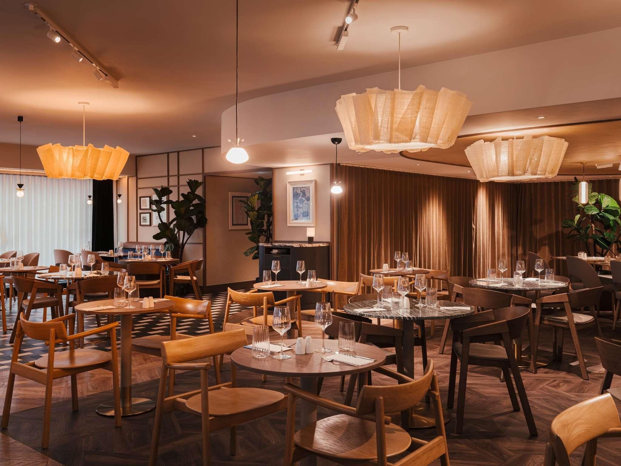 A restaurant with round tables and chairs, overhead lighting, and a checkered floor.