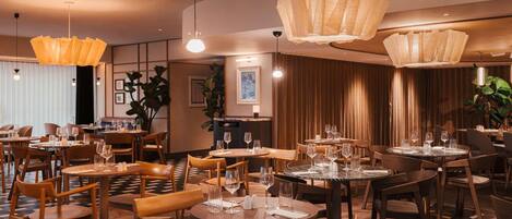 A restaurant with round tables and chairs, overhead lighting, and a checkered floor.