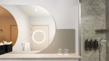 A modern bathroom with a large mirror, a shower, and toiletries on the wall.
