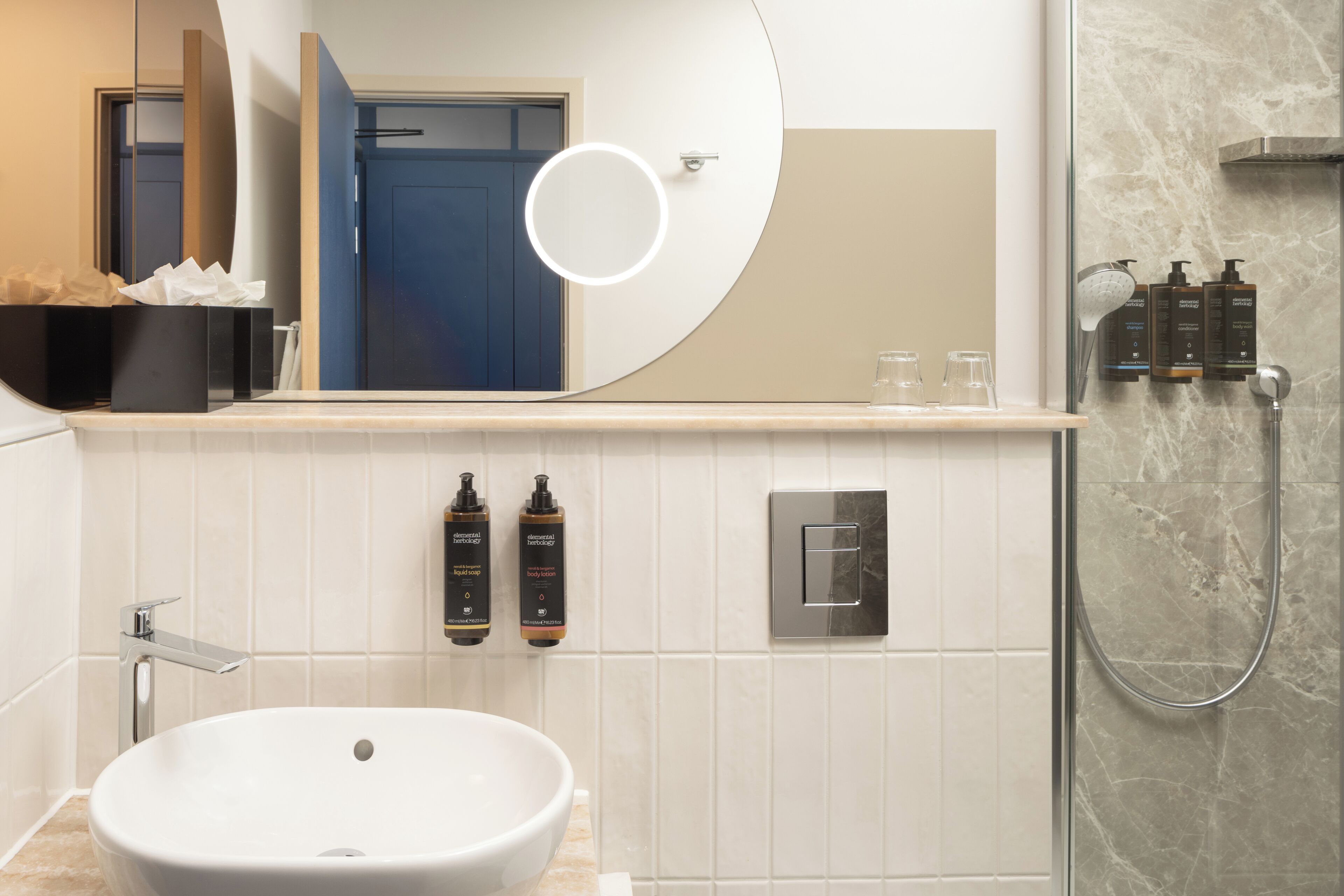 Une salle de bain moderne avec un lavabo blanc, un miroir doté d’un éclairage circulaire et un espace douche.