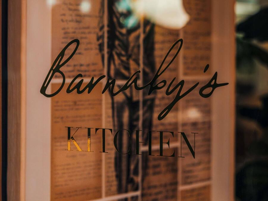 Een lijst met een bord waarop staat 'Barnaby's KITCHEN' en een deel van een plantje is te zien.