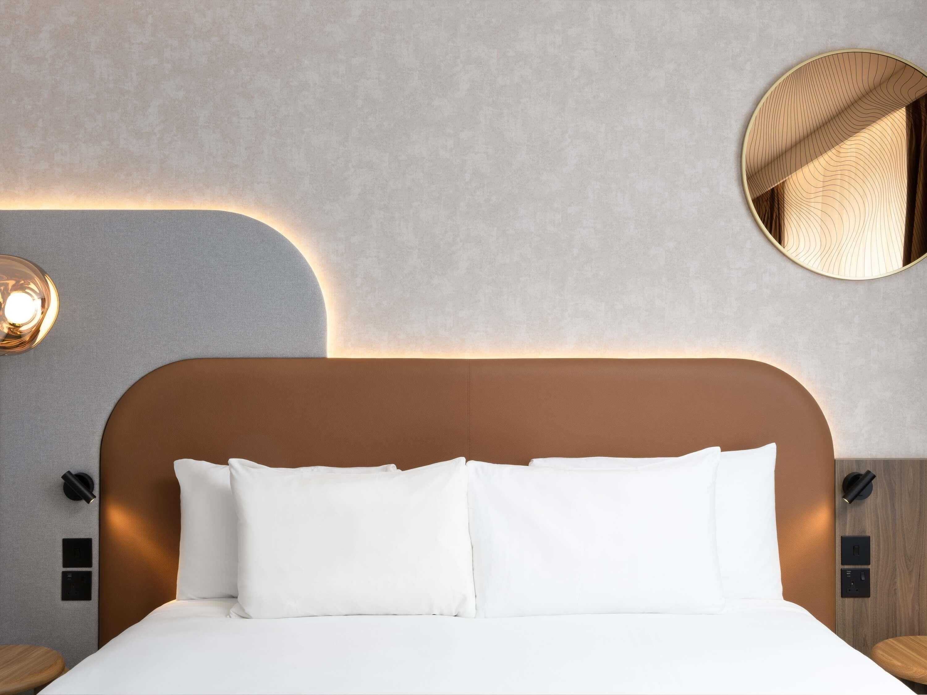 A modern hotel room with a large bed, a round mirror, and wall-mounted lighting.